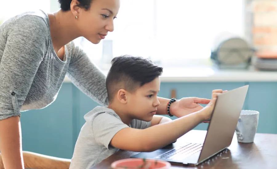 A mother helps her son with his coding on a laptop at home