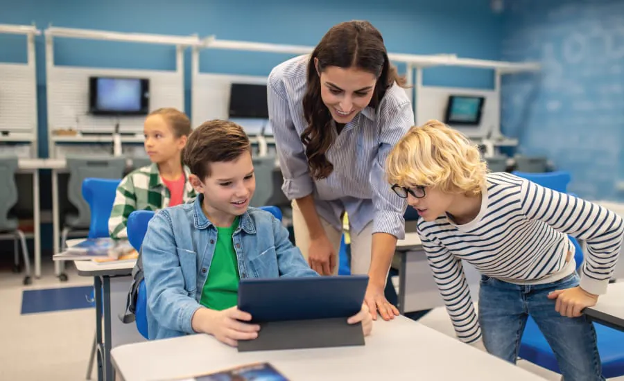 A teacher helps two boys with their coding work on tablets in a classroom