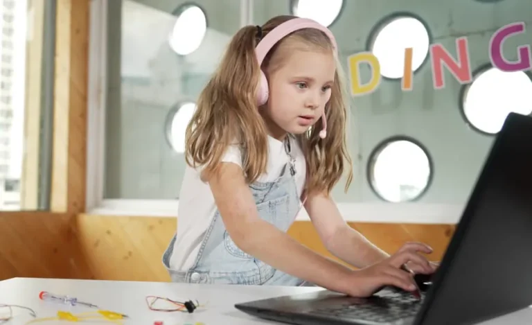 A girl in headphones types code on her laptop in a bright classroom