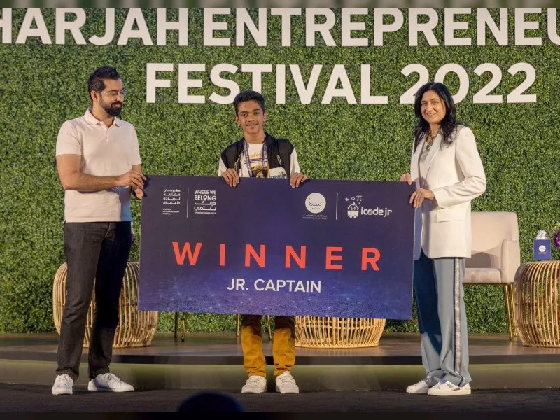 The Grades 1–4 CodeNova champion holds a winner's sign larger than herself on stage at SEF 2022