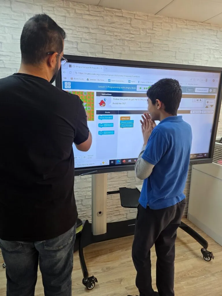 An iCodejr instructor works with a student on a Scratch project at the classroom screen at Behaviour Enrichment