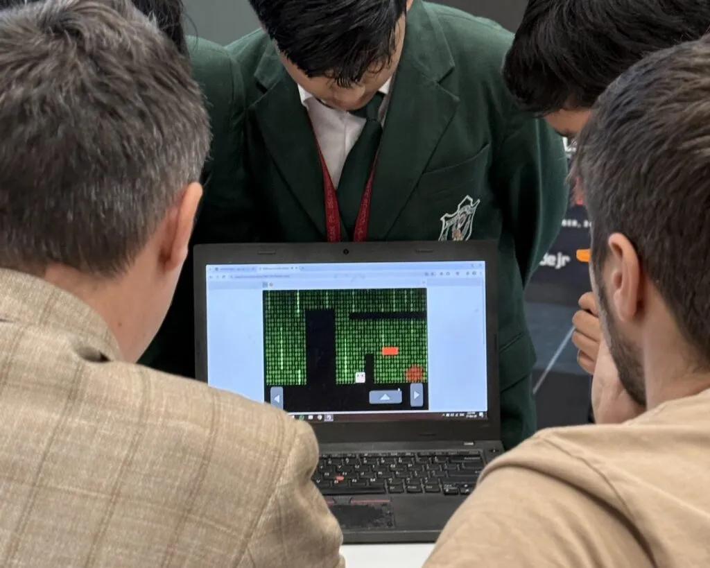 Students lean over a laptop to show two judges the game they coded